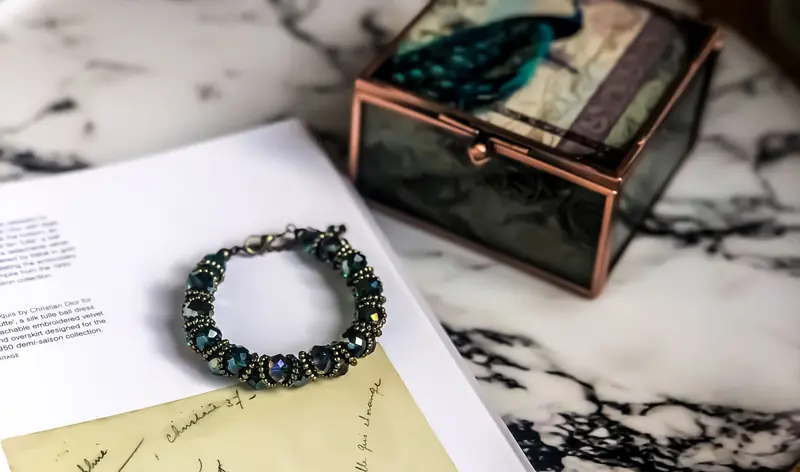 A close-up of a stylish gemstone bracelet resting on a marble surface beside a decorative box