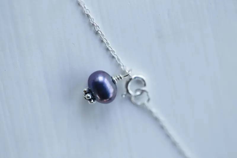 Close-up of a silver necklace with a purple pearl pendant, showcasing fine details