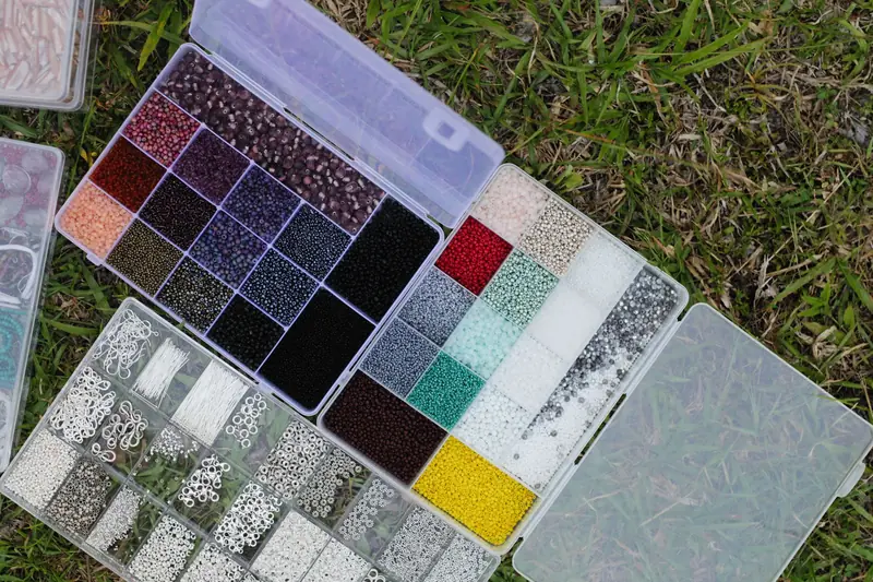 Top view of colorful beads organized in plastic boxes on grassy ground, ideal for crafting and hobbyists