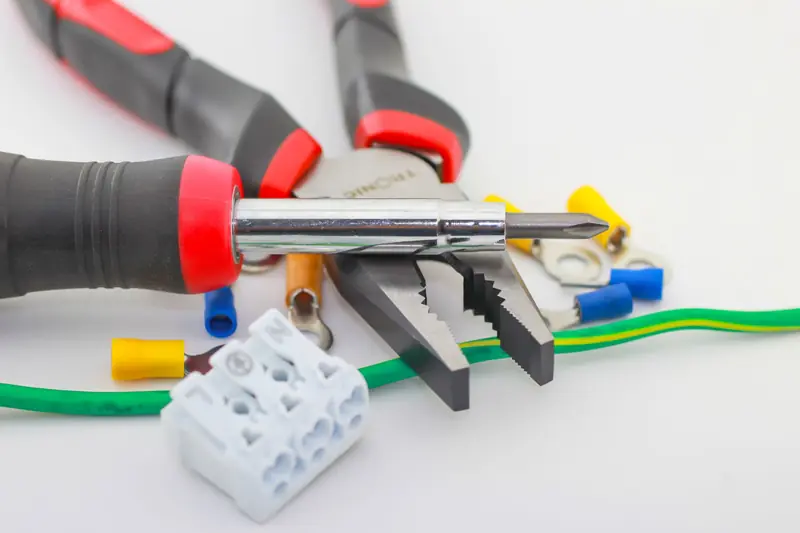 A detailed close-up of hand tools including a screwdriver and pliers with various wiring accessories