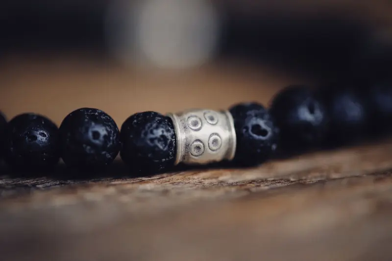 Detailed close-up of a beaded bracelet with dark textured beads and a decorative metal accent piece
