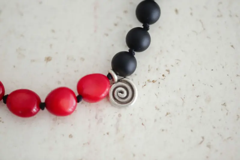 Detailed close-up of a stylish red and black beaded bracelet with a spiral charm