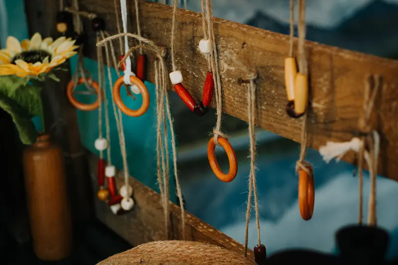 A rustic display of handmade beaded and wooden jewelry hanging outdoors on twine