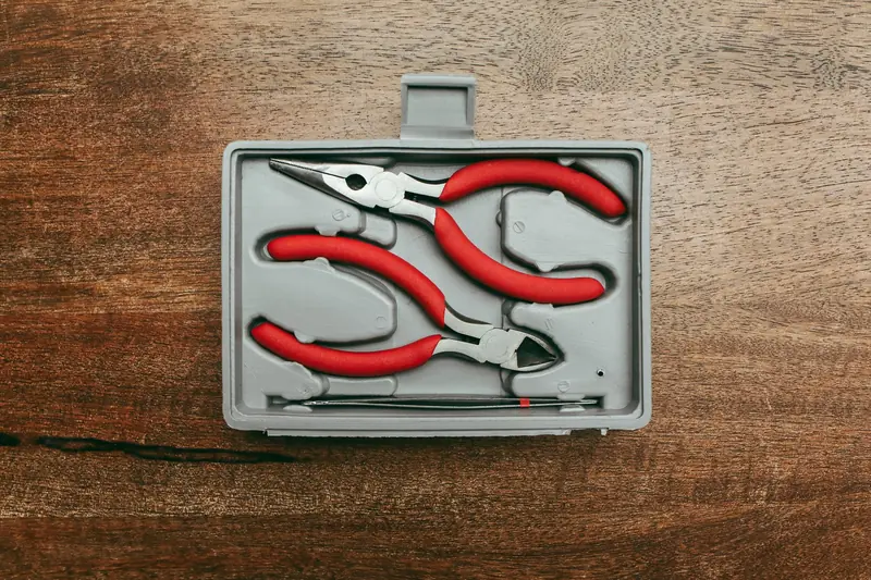 Top view of a red handled pliers set in a box on a wooden surface