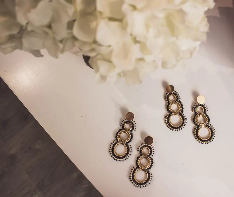 Stylish beaded earrings with circular design on a white surface, surrounded by soft flowers