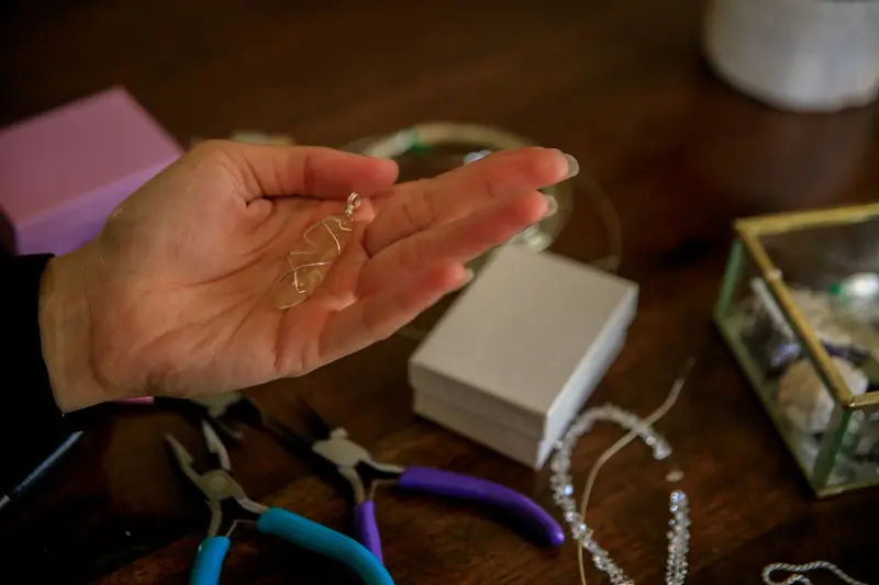 Close-up of a hand holding a crystal pendant surrounded by jewelry tools