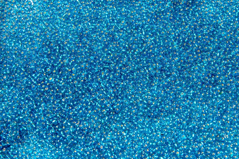 Detailed close-up of a pile of vibrant blue glass seed beads, highlighting texture and color