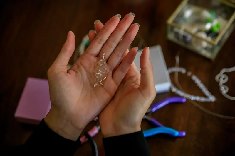 Close-up of hands presenting a handmade silver wire pendant with jewelry tools on a wooden table