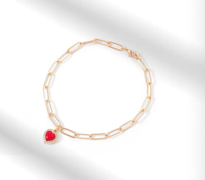 Close-up of a gold chain bracelet featuring a heart-shaped red gemstone pendant, ideal for elegant soirées