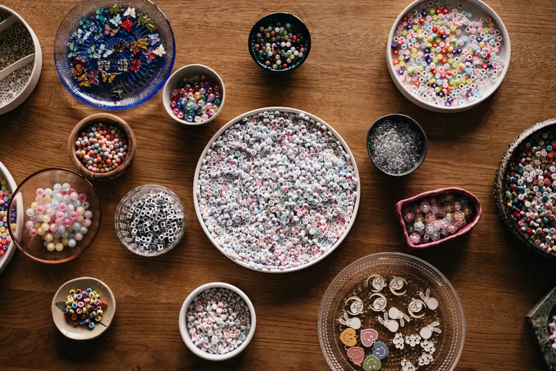 A top view of assorted colorful beads in bowls on a wooden table, ideal for arts and crafts